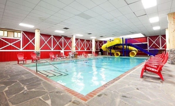 Image of the Pine Ridge Dude Ranch all-inclusive family dude ranch vacation indoor pool surrounded by a flagstone paver deck with red chairs and a yellow double water slide.